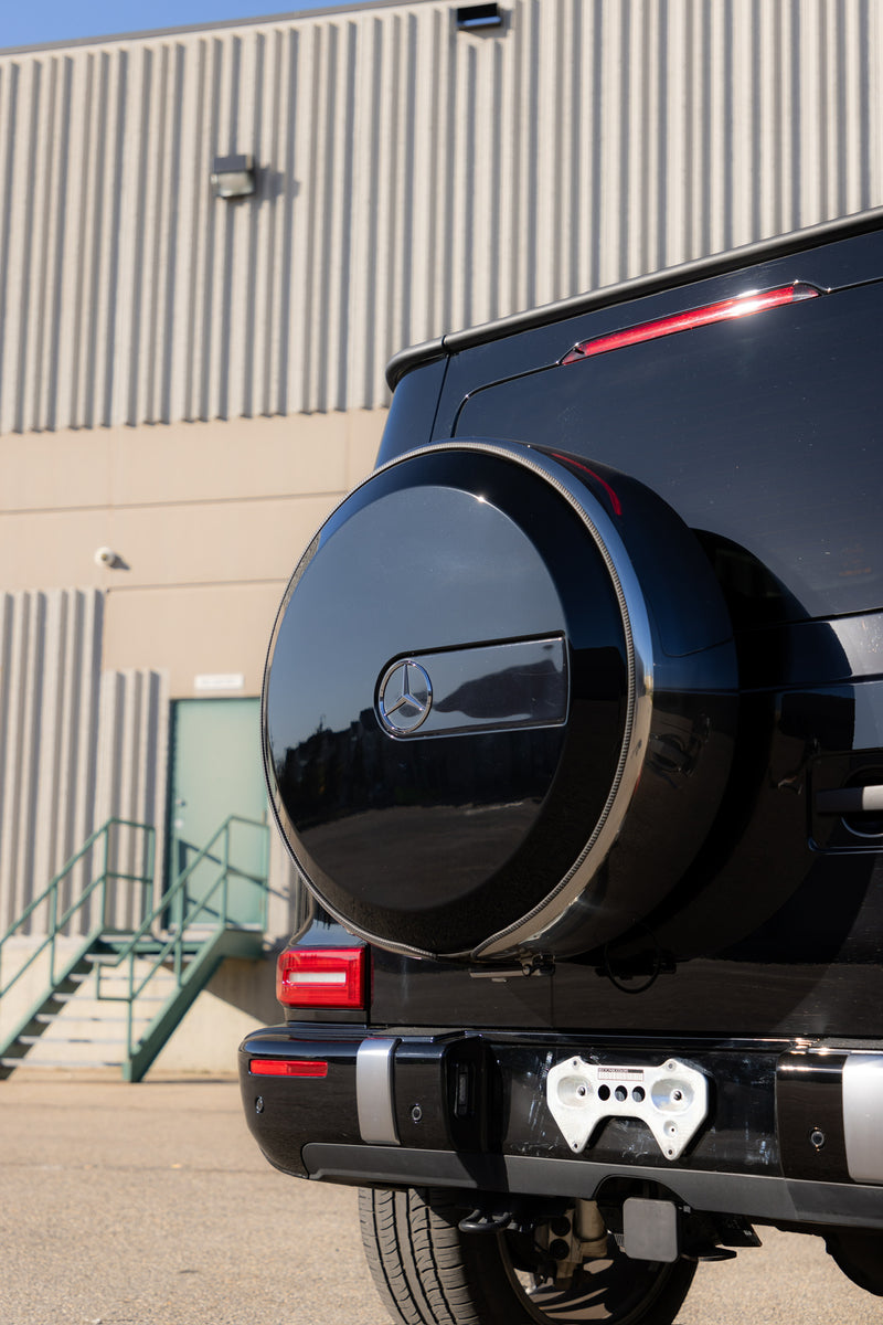 Gloss black wrapped G-wagon with a spare tire mounted on the back, parked in front of a building.