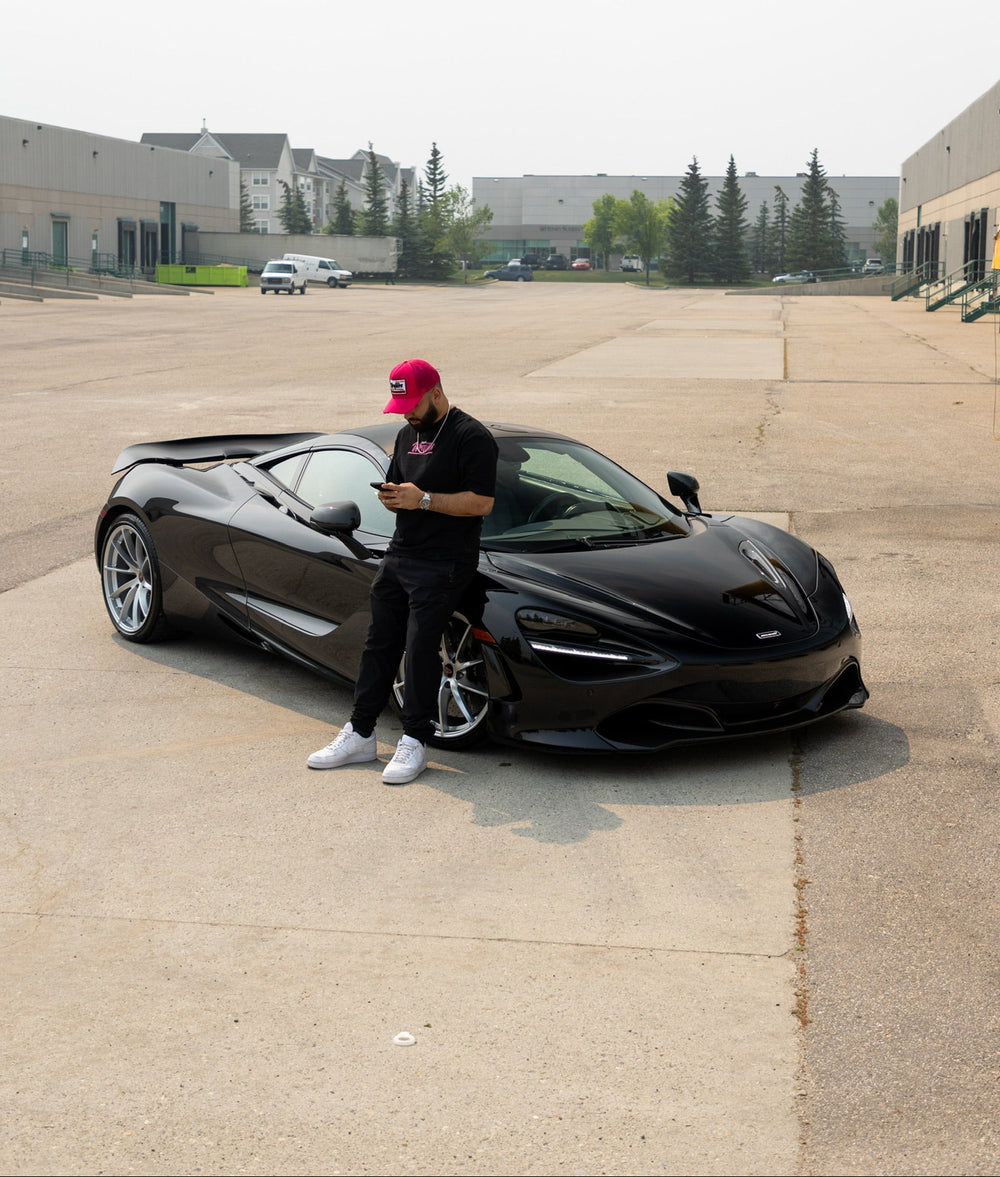 Wraptors Calgary Owner standing next to a wrapped gloss black McLaren in an open area with buildings in the background