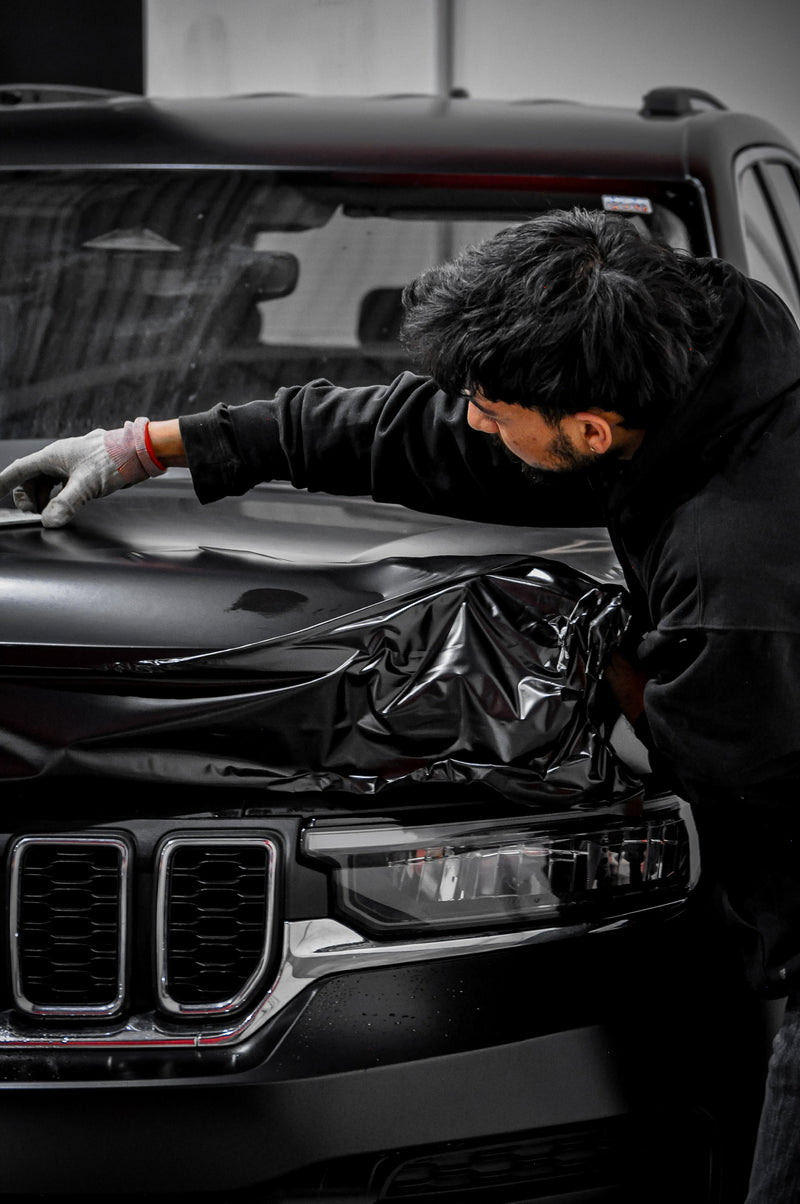 Professional installer applying matte black vinyl wrap to SUV hood during a vehicle wrap installation at wraptors calgary