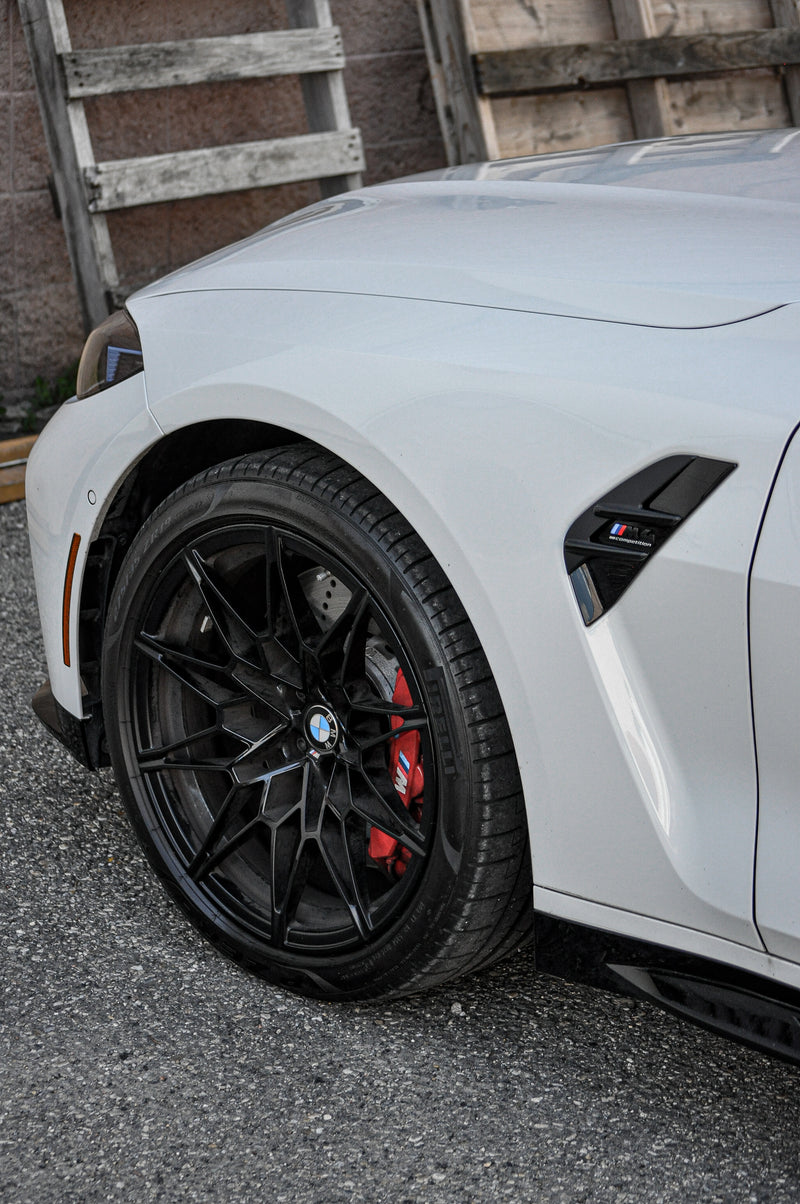 Close-up of a white car's wheel with powdercoated black rim and powdercoated red calipers on a textured wall background.