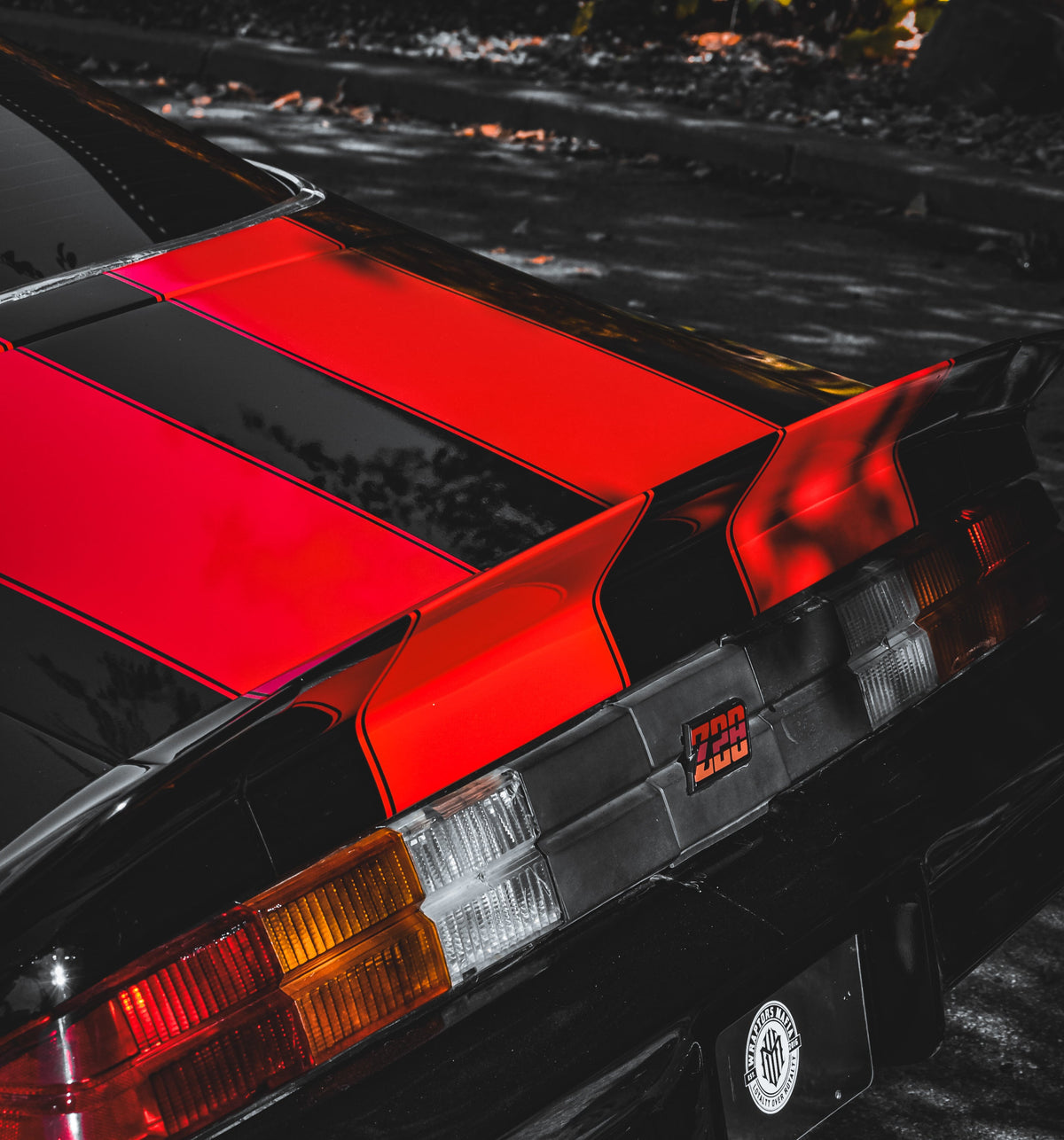 Close-up of a car's rear end with vinyl red and black racing stripe design, on a dark background.