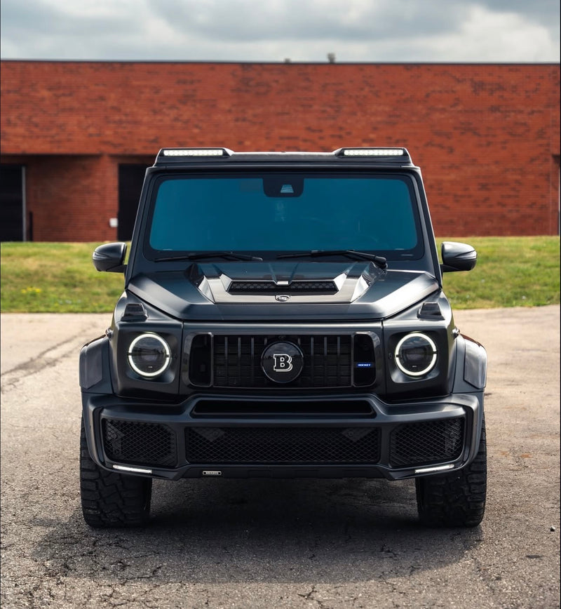 A coloured ppf wrap on a black luxury SUV with a brand logo on a paved surface and grassy area in the background.