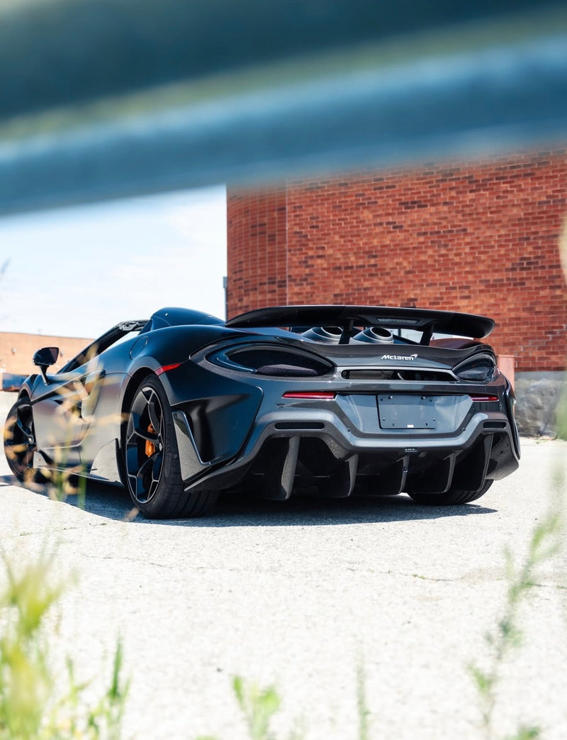 Black McLaren sports car parked on a gravel driveway with a brick wall in the background, full vehicle coloured ppf and ceramic coating completed