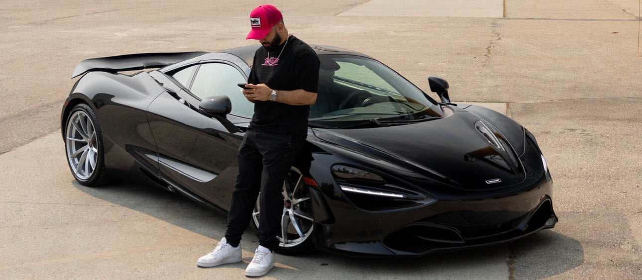 Person standing next to a black sports car on an open area