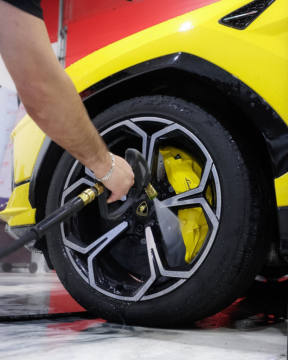 Detailer pressure washing Lamborghini wheel and brake calipers during a professional luxury vehicle  detailing service at Wraptors Calgary